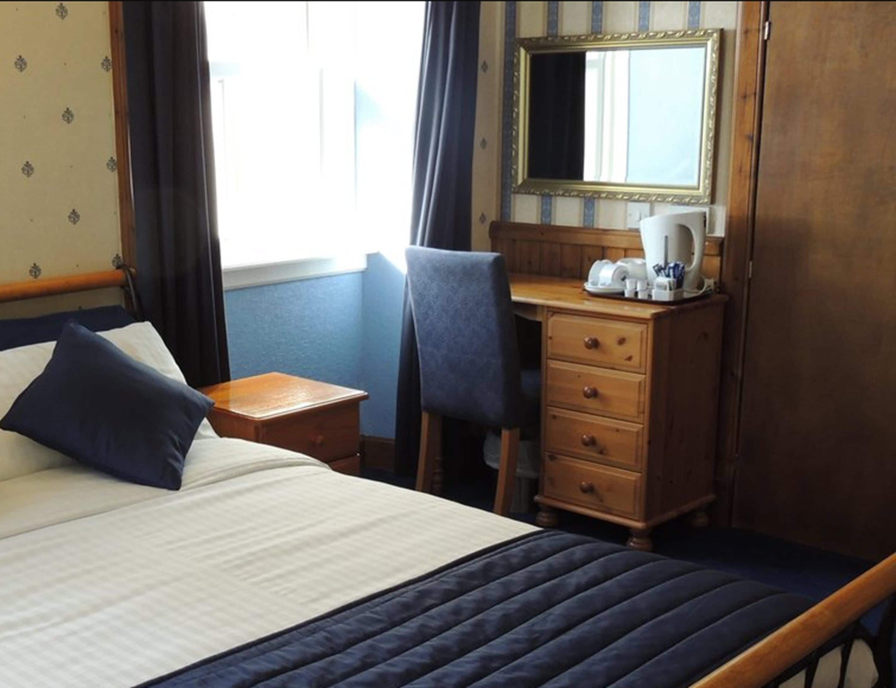Habitación de hotel con una cama, un escritorio, una silla, un aparador y un espejo.