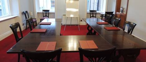 Une salle de conférence avec une longue table, des chaises noires et des sets de table rouges.