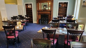 A dining area with wooden tables and chairs, a fireplace, and a bookshelf in the background. - The Orkney Hotel (Kirkwall)