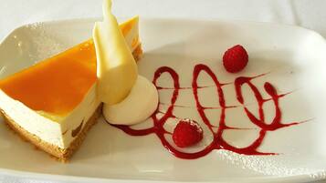 A dessert plate with a slice of cheesecake, a scoop of vanilla ice cream, and raspberry sauce.