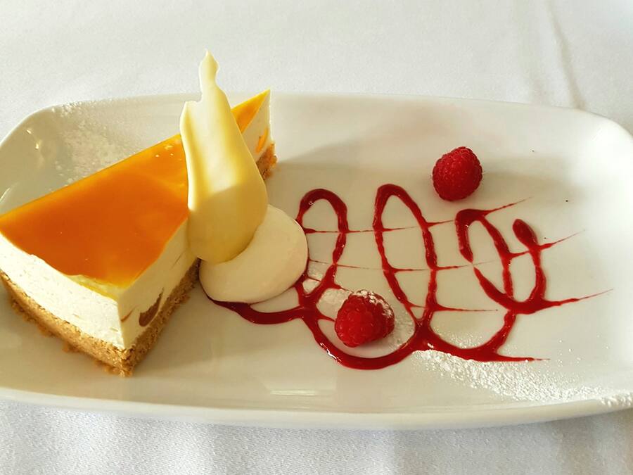 A dessert plate with a slice of cheesecake, a scoop of vanilla ice cream, and raspberry sauce.