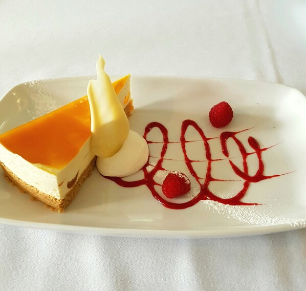 A dessert plate with a slice of cheesecake, a scoop of vanilla ice cream, and raspberry sauce.