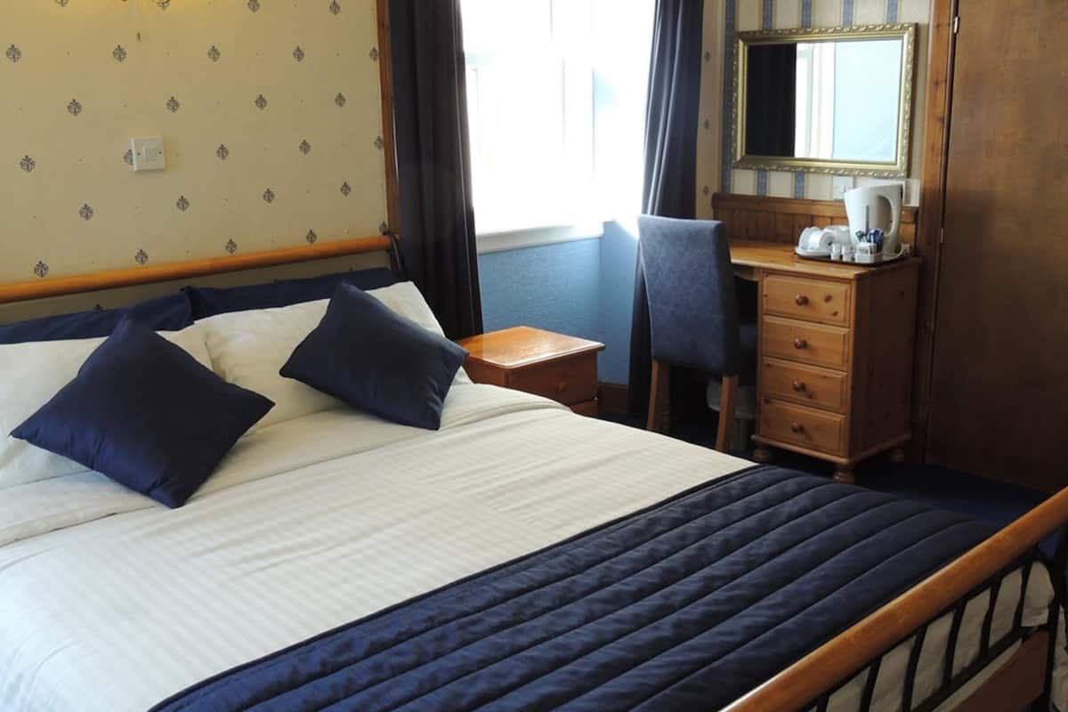 A neatly made bed with dark blue bedding, a wooden headboard, and a bedside table with a lamp and a cup.