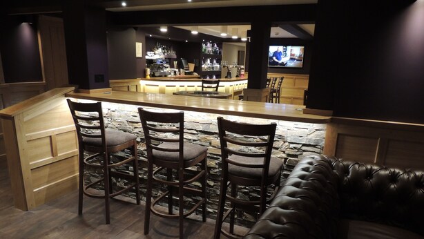 A bar area with a stone wall, wooden bar counter, and bar stools. There is a leather couch in the foreground. - The Orkney Hotel (Kirkwall)