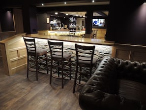 A bar area with a stone wall, wooden bar counter, and bar stools. There is a leather couch in the foreground. - The Orkney Hotel (Kirkwall)