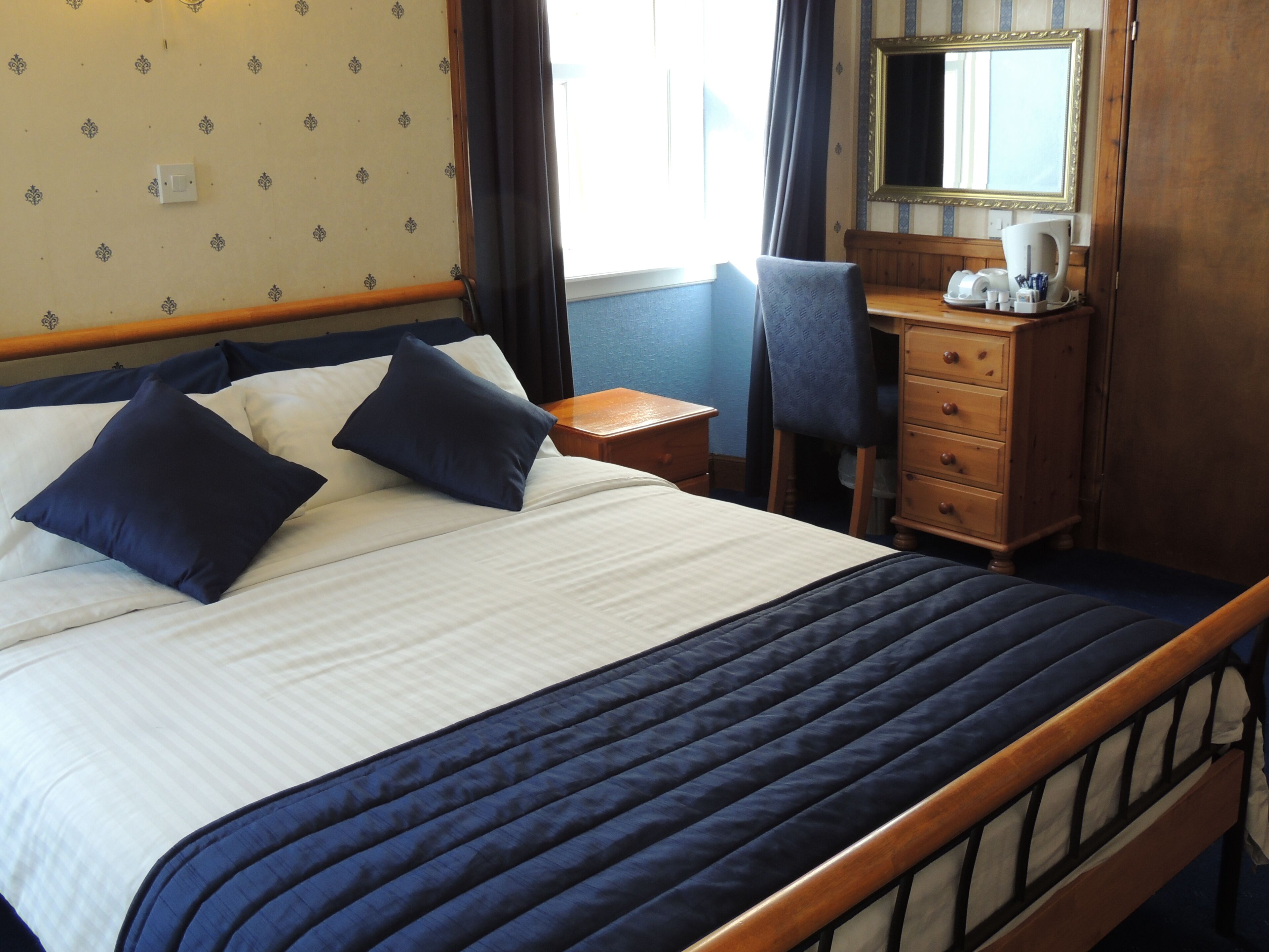 Una habitación de hotel con cama, escritorio, silla, cómoda y espejo.