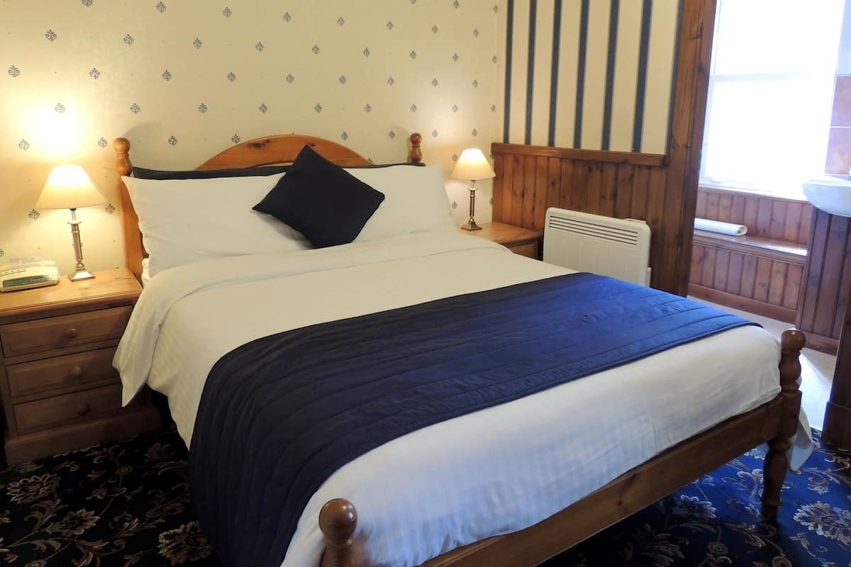 A neatly made bed with a wooden headboard, two bedside lamps, and a patterned wall.