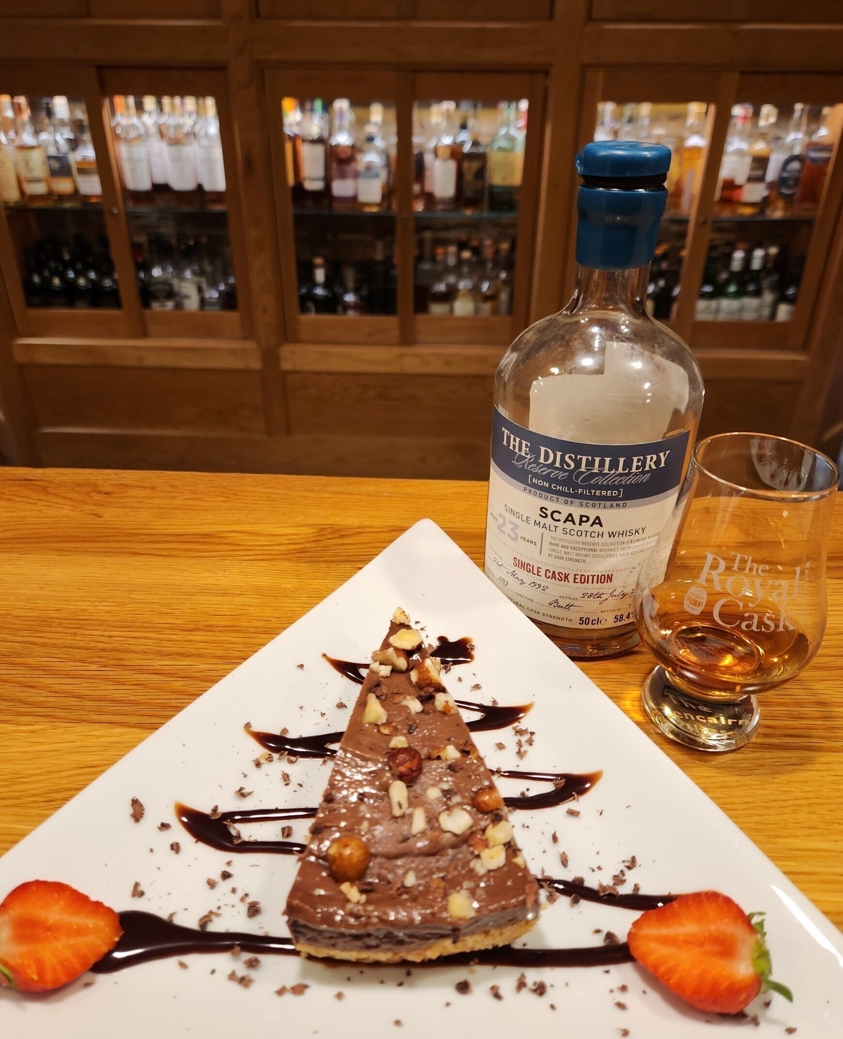 Ein Dessertteller mit Schokolade und Erdbeeren, eine Flasche schottischer Whisky und ein Glas auf einem Holztisch.