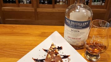 Ein Dessertteller mit Schokolade und Erdbeeren, eine Flasche schottischer Whisky und ein Glas auf einem Holztisch.