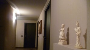 Ein Flur mit einer Tür am Ende, einem Kamin mit zwei weißen Statuen und einer Wandleuchte.