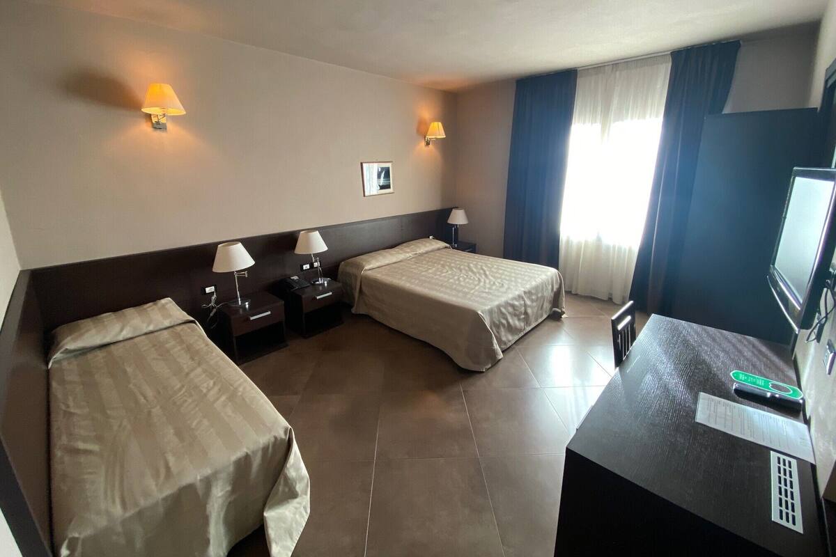 Ein Hotelzimmer mit zwei Einzelbetten, einem Schreibtisch mit Fernseher und einem Fenster mit Vorhängen.