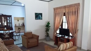 Uma sala de estar com dois sofás, uma televisão, uma planta e um espaço de jantar com mesa e cadeiras.