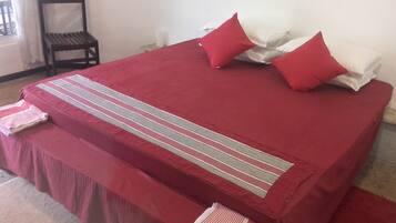 Una cama bien tendida con una colcha roja, dos almohadas rojas y una almohada a rayas sobre una funda de almohada blanca.