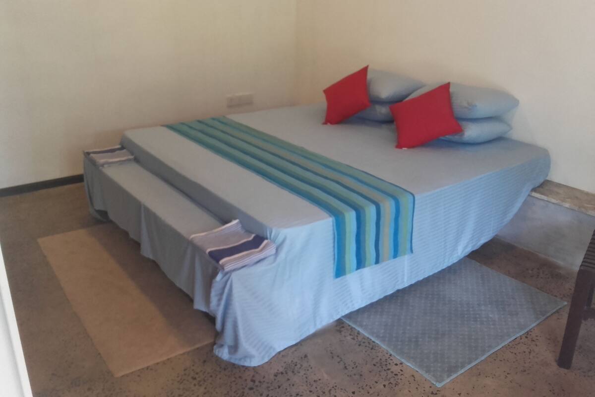 A bed with a blue and white striped bedspread, red and blue pillows, and a grey blanket.