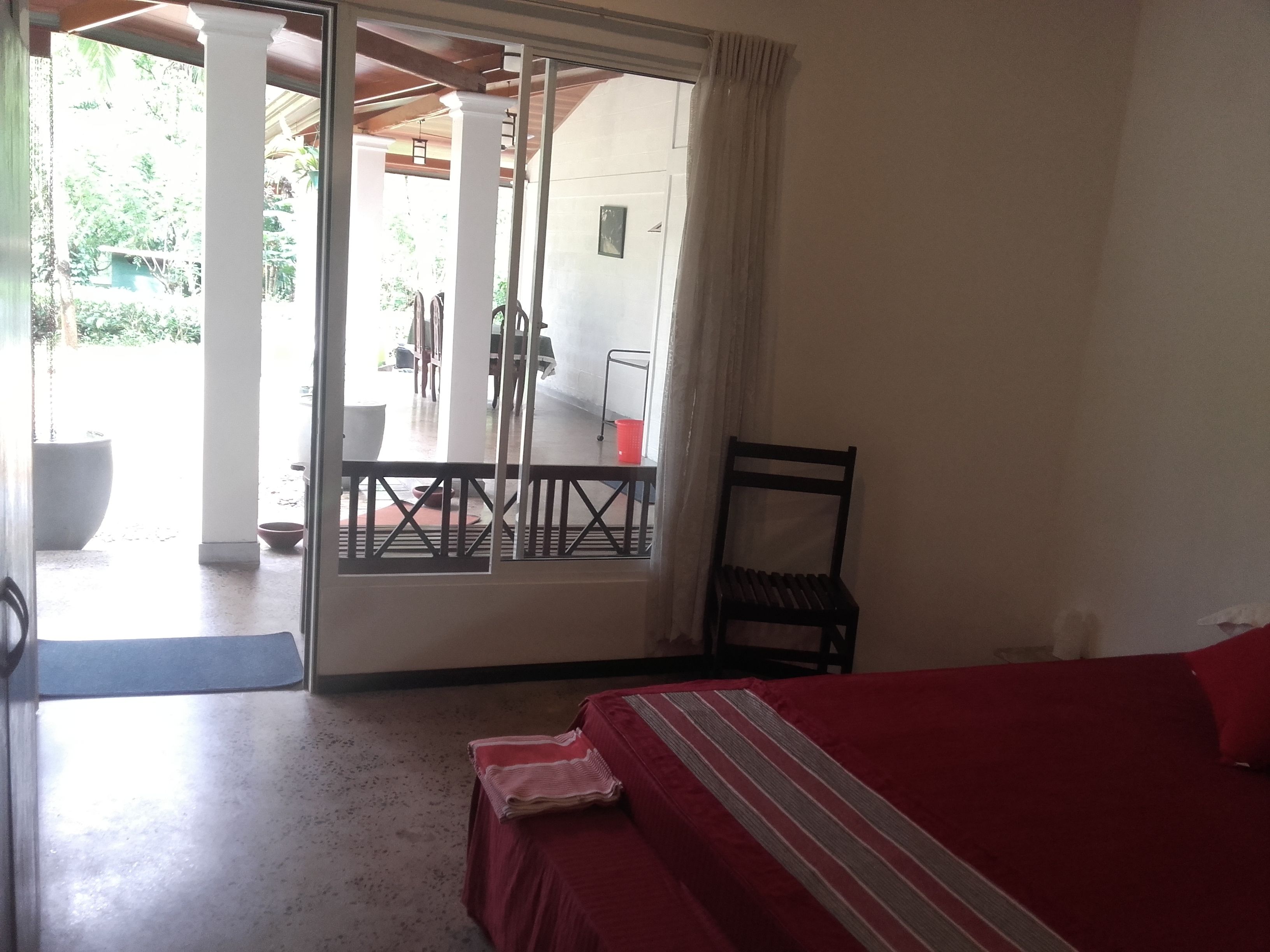A room with a bed, a chair, a table, and a view of an outdoor area with a balcony.