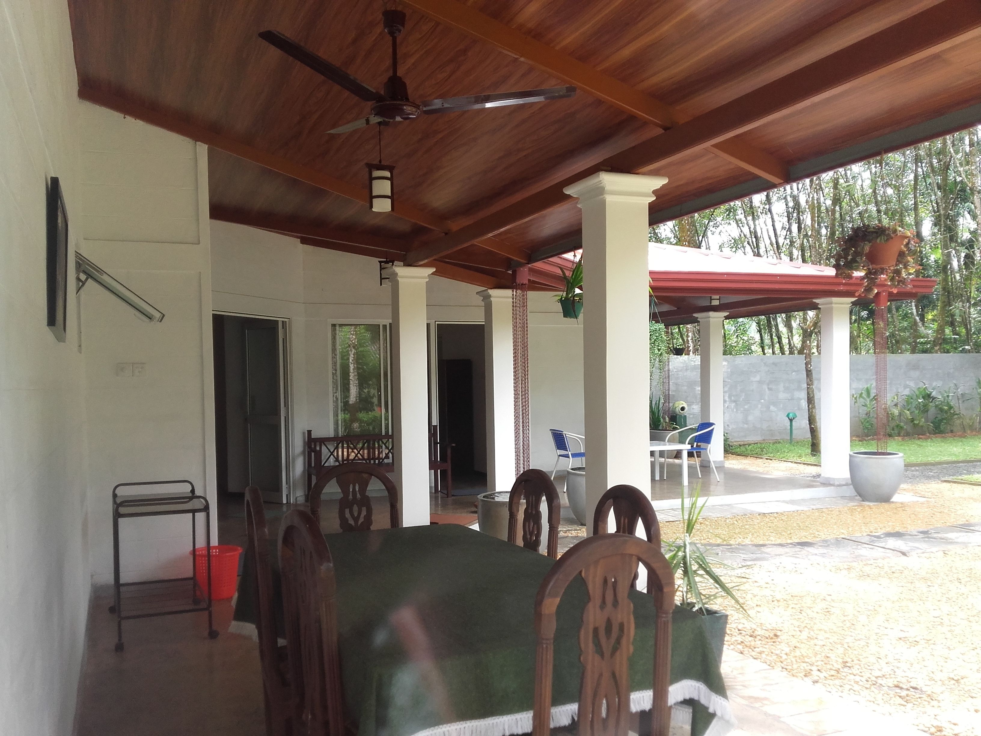A covered outdoor dining area with a ceiling fan, wooden chairs, and a table with a green tablecloth.