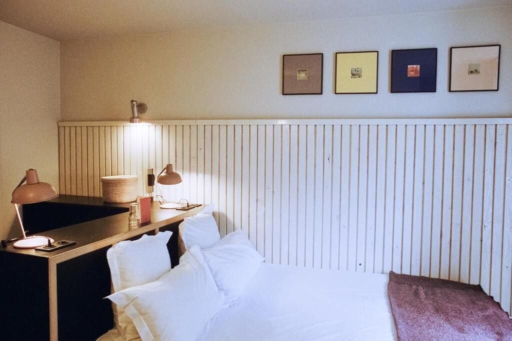 A hotel room with a bed, bedside table, lamp, and wall-mounted pictures.