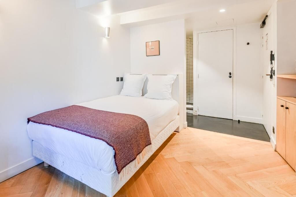Um quarto com cama, porta e piso de madeira.