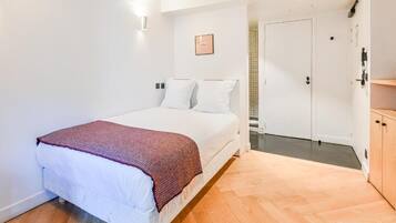 Um quarto com cama, porta e piso de madeira.