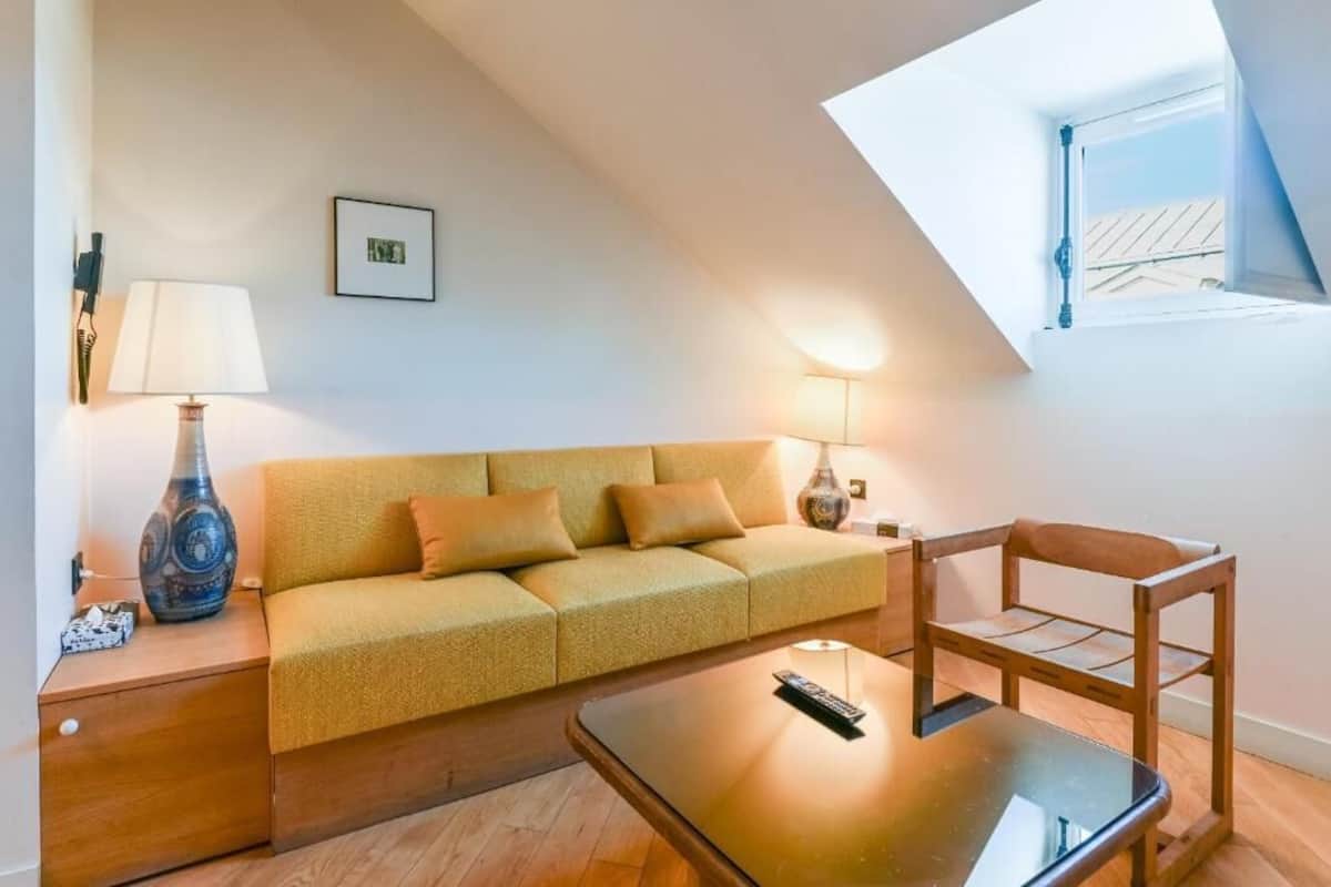 A cozy living room with a sofa, a coffee table, a lamp, and a small table with a remote control.