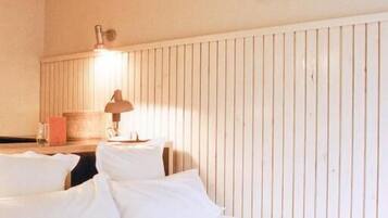A hotel room with two beds, a wooden headboard, a lamp, and two framed pictures on the wall.