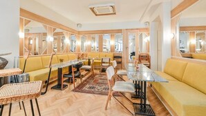 A dining area with yellow sofas, mirrored walls, and a central table. - Hôtel Habituel (Paris)
