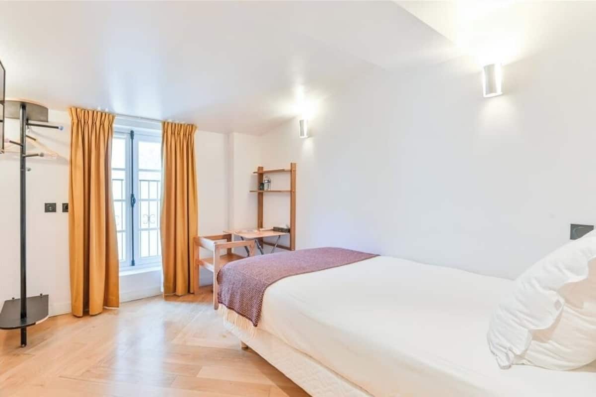 A bedroom with a bed, a desk, a chair, a window with curtains, and a shelf.