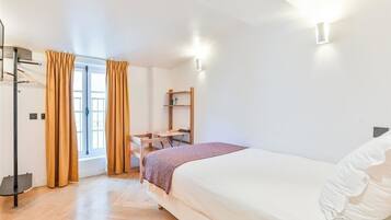 Ein Schlafzimmer mit Bett, Schreibtisch, Stuhl, einem Fenster mit Vorhängen und einem Regal.