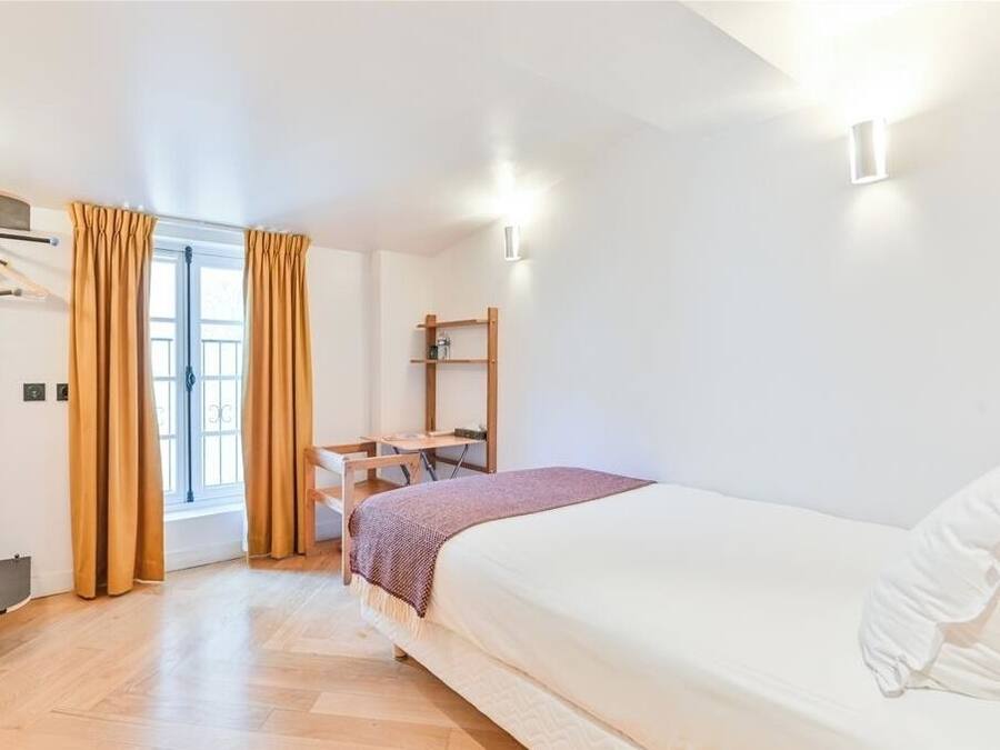 Ein Schlafzimmer mit Bett, Schreibtisch, Stuhl, einem Fenster mit Vorhängen und einem Regal.