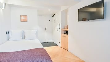 Una habitación de hotel moderna con una cama, un televisor montado en la pared, un armario de madera y una puerta que da al baño.