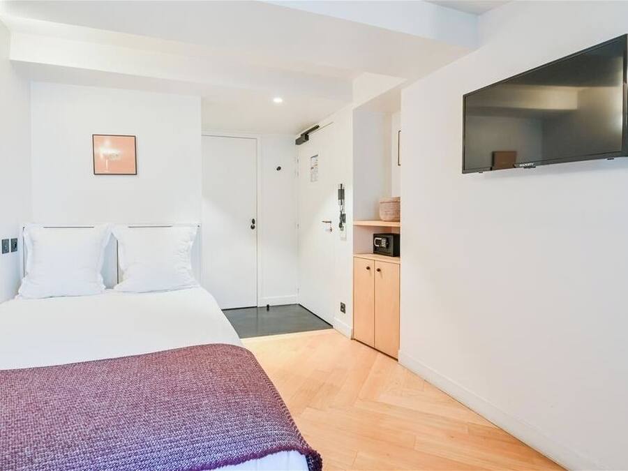 Una habitación de hotel moderna con una cama, un televisor montado en la pared, un armario de madera y una puerta que da al baño.