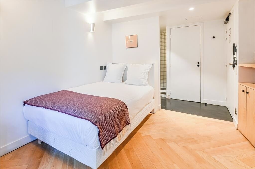 A bedroom with a bed, a door, and a wooden floor.