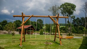 A wooden swing set in a grassy park with a small building in the background. - Drevenice TriMount (Bobrovec)