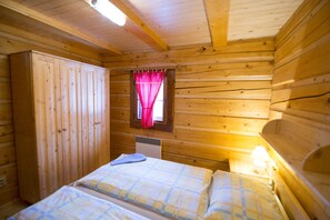 A wooden cabin room with two beds, a wardrobe, a window with red curtains, and a nightstand with a lamp. - Drevenice TriMount (Bobrovec)
