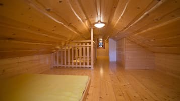 A wooden attic bedroom with a bed, a white railing, and a staircase leading to a loft area.