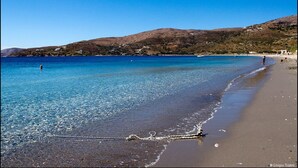 Uma praia com águas azul-claras, areal arenoso e colinas ao fundo.