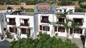 Um hotel com uma placa que diz 'Maestralias', com um navio e ondas. Possui várias varandas com grades de madeira e paredes brancas.