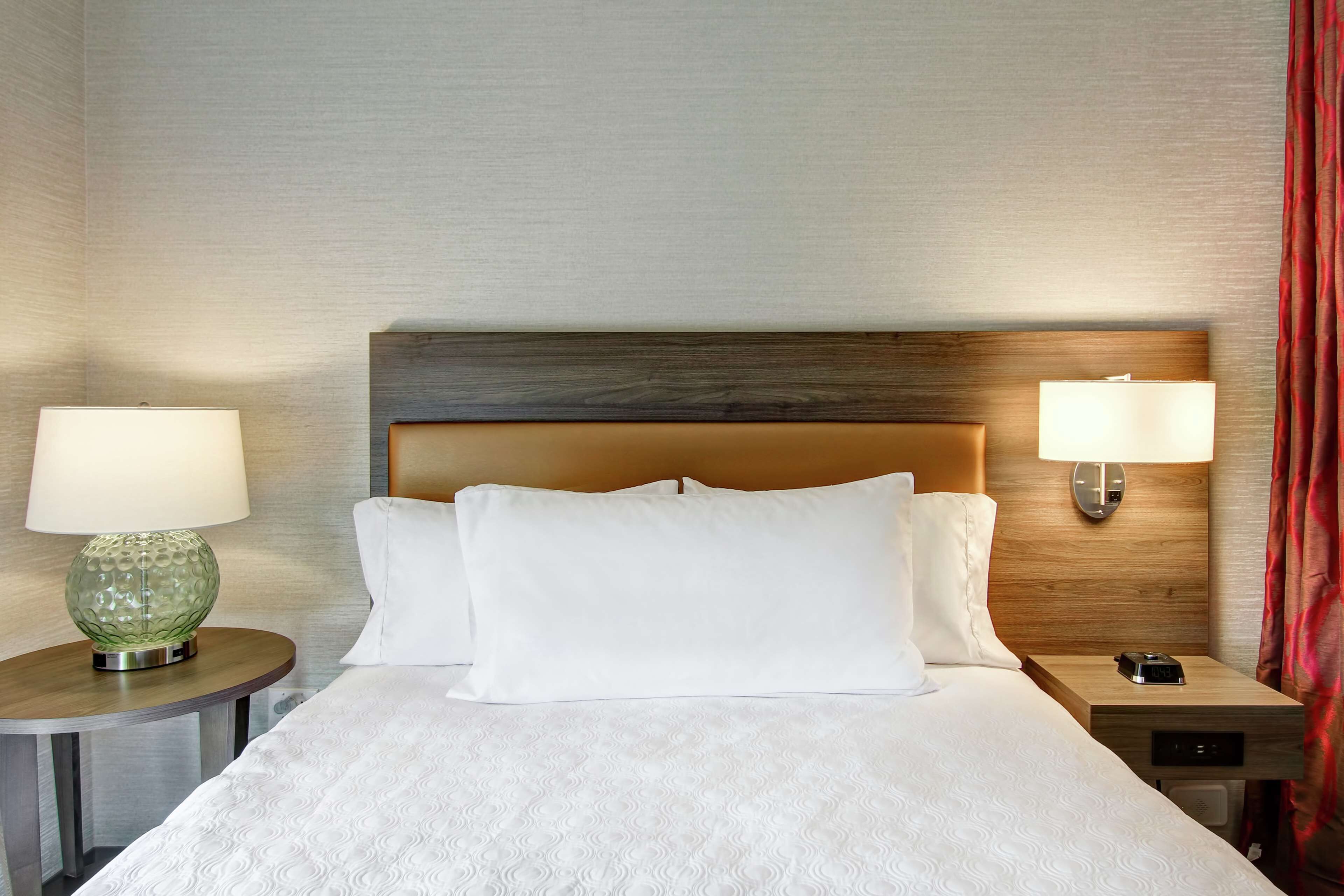 A hotel room with a large bed, two bedside tables, and two wall-mounted lamps.