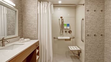 A modern bathroom with a vanity, a shower with a glass door, and a toilet with grab bars.
