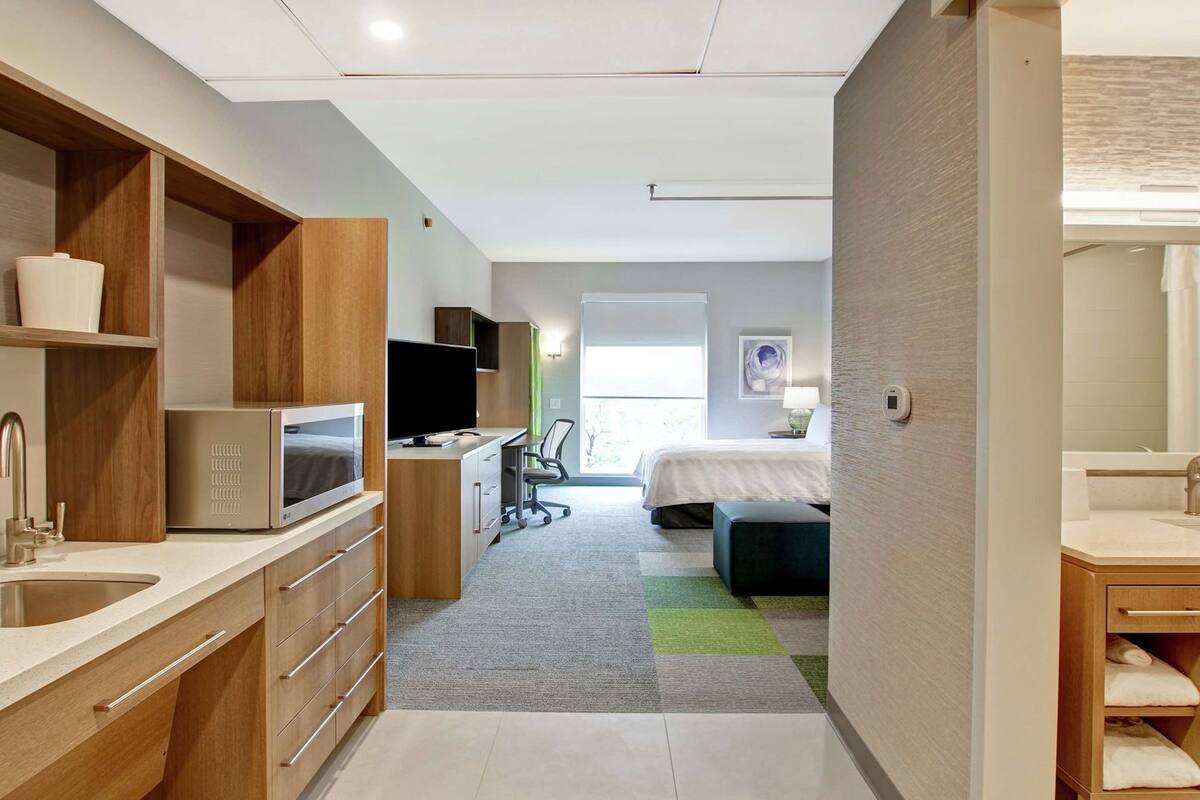 Een moderne hotelkamer met kitchenette, een bed, een bureau en een badkamer.