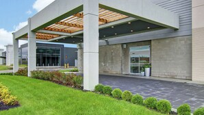 Een modern gebouw met een overdekte entree, een verharde oprit en een aangelegde tuin.