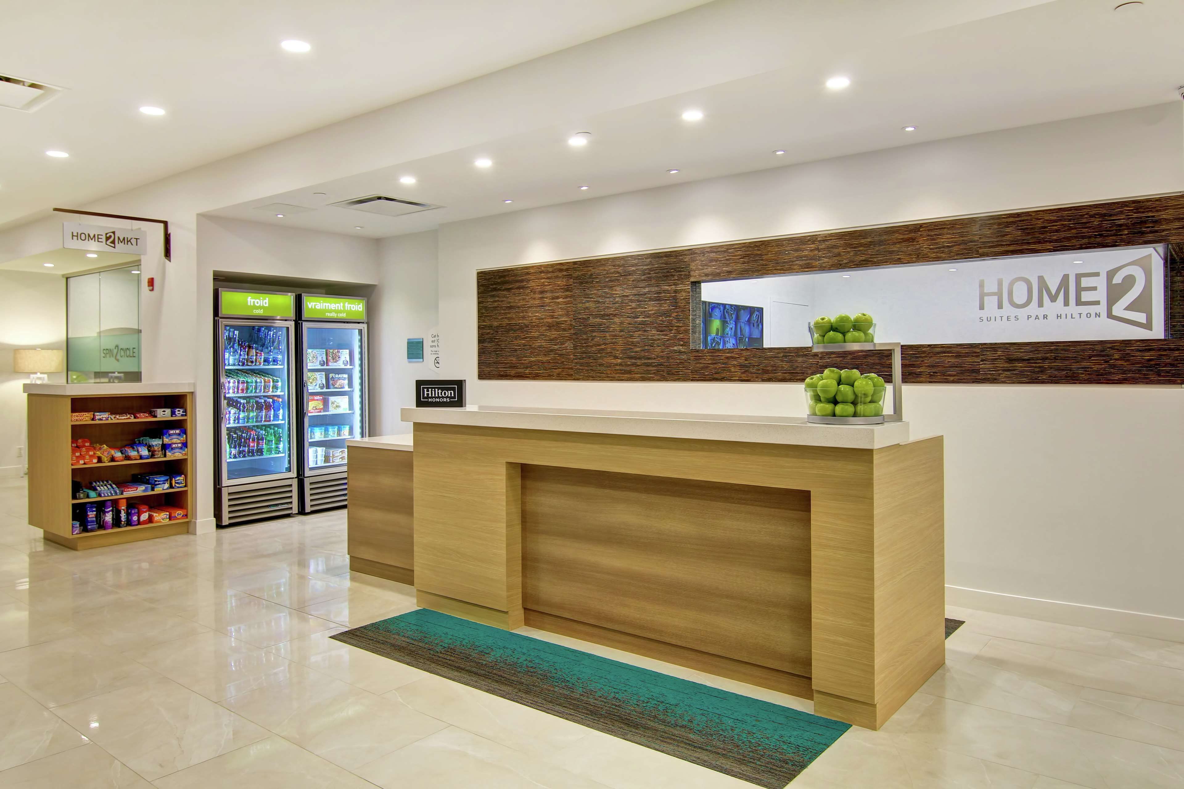 A hotel reception area with a wooden reception desk, a digital screen, and a minibar.