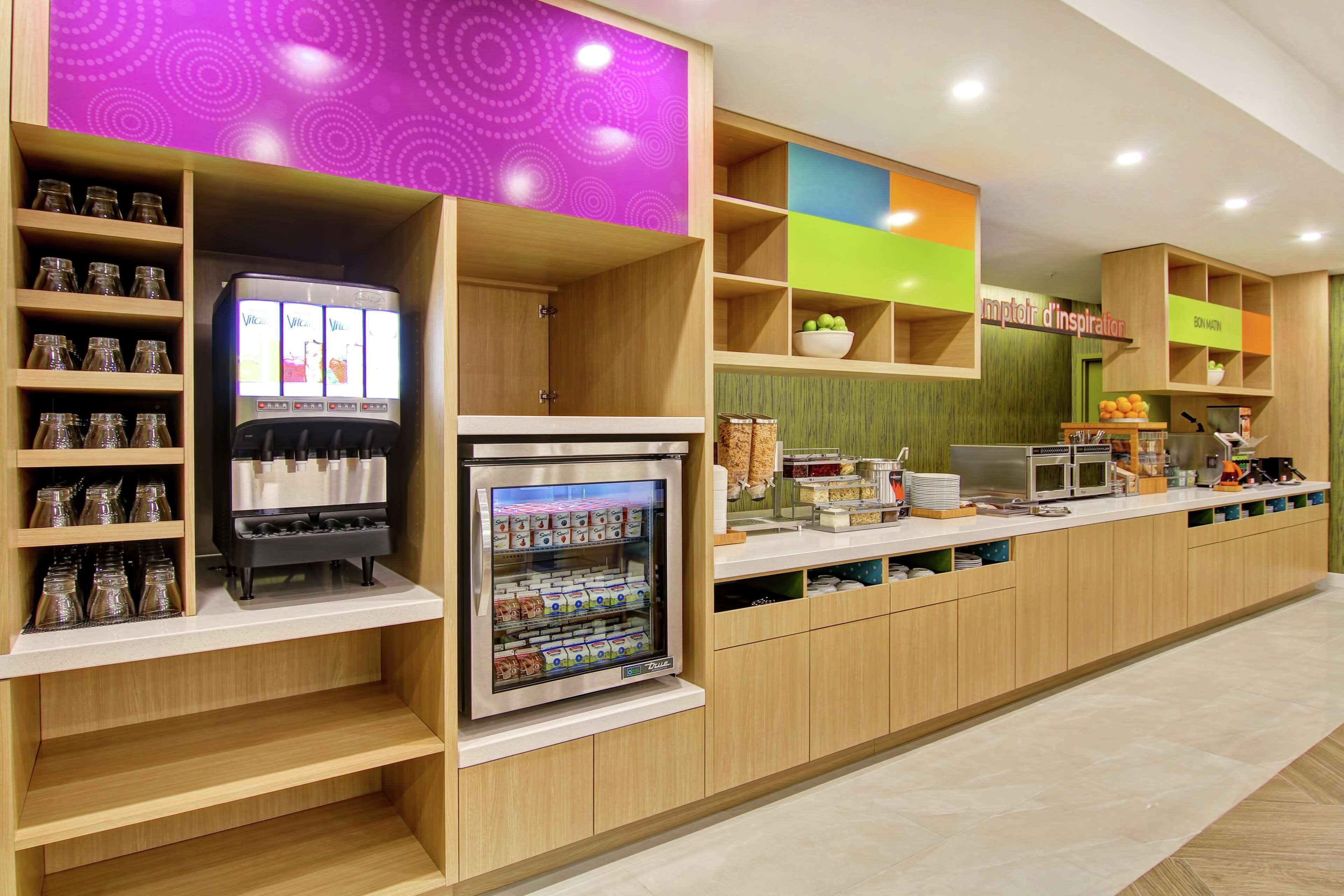 Un espace cuisine moderne comprenant un coin boissons en libre-service, un réfrigérateur contenant divers aliments et un comptoir équipé d’ustensiles de cuisine.