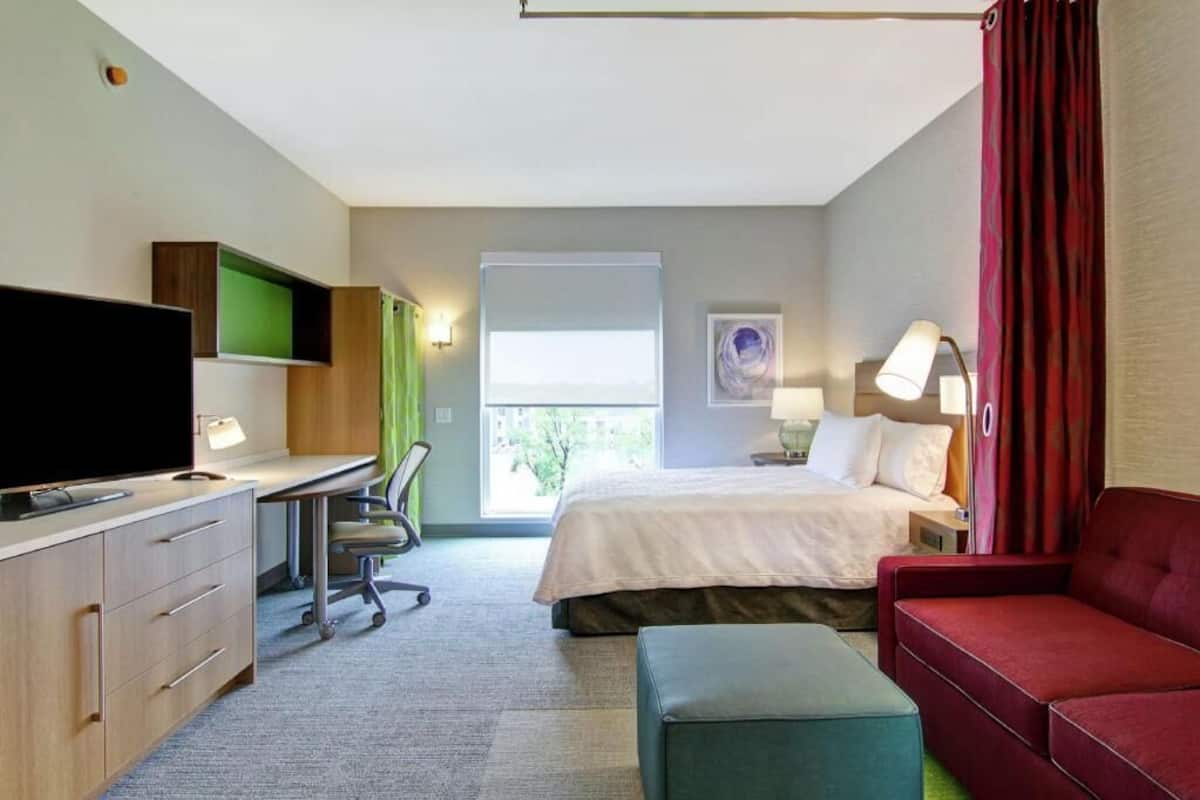 Een hotelkamer met een bed, bureau, televisie en een rode bank.