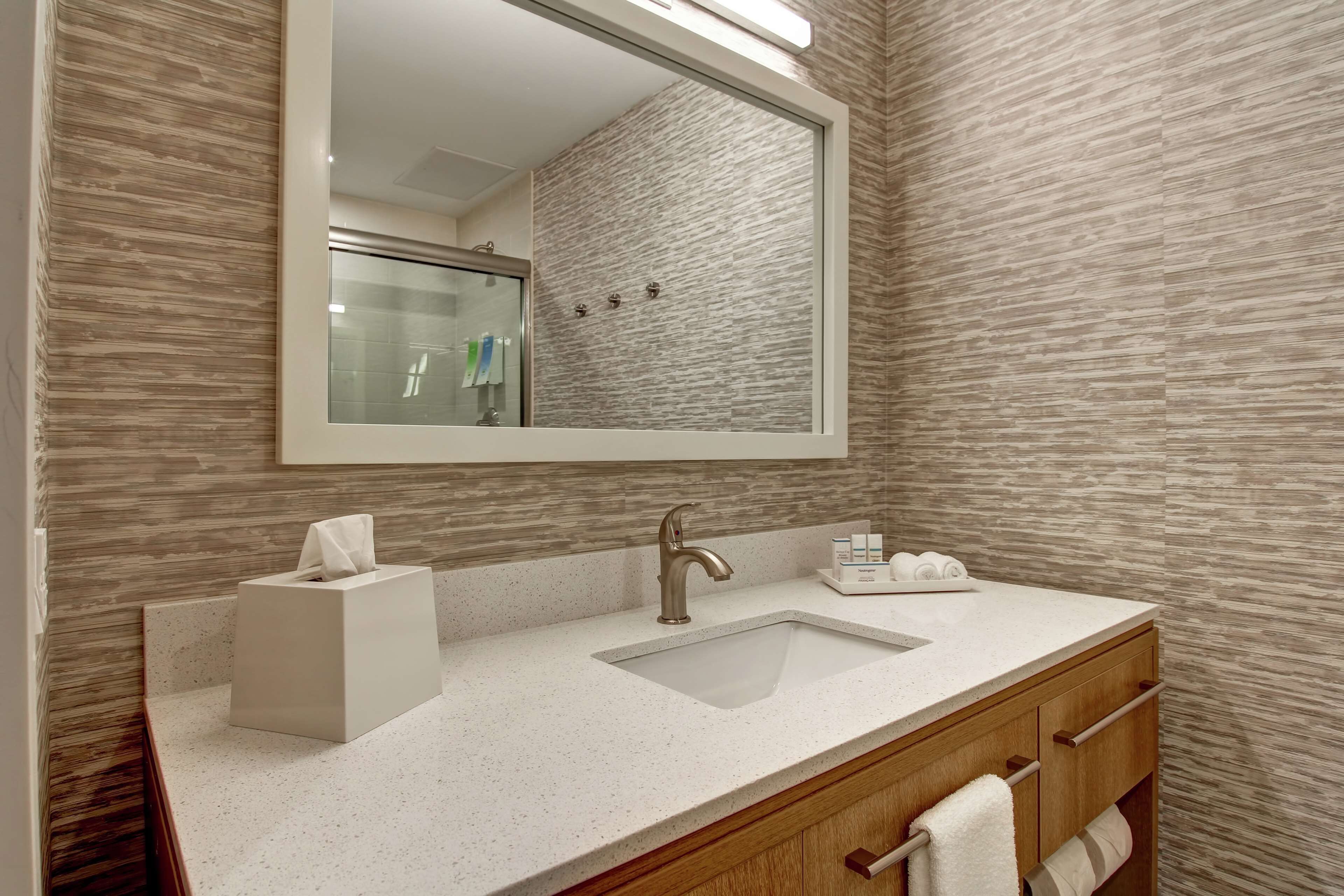 Un baño moderno con un espejo grande, un lavabo y un mueble de tocador con un perchero para toallas.