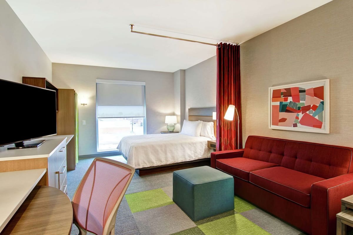 Een hotelkamer met een bed, een rode bank, een televisie, een bureau en een kleurrijk vloerkleed.