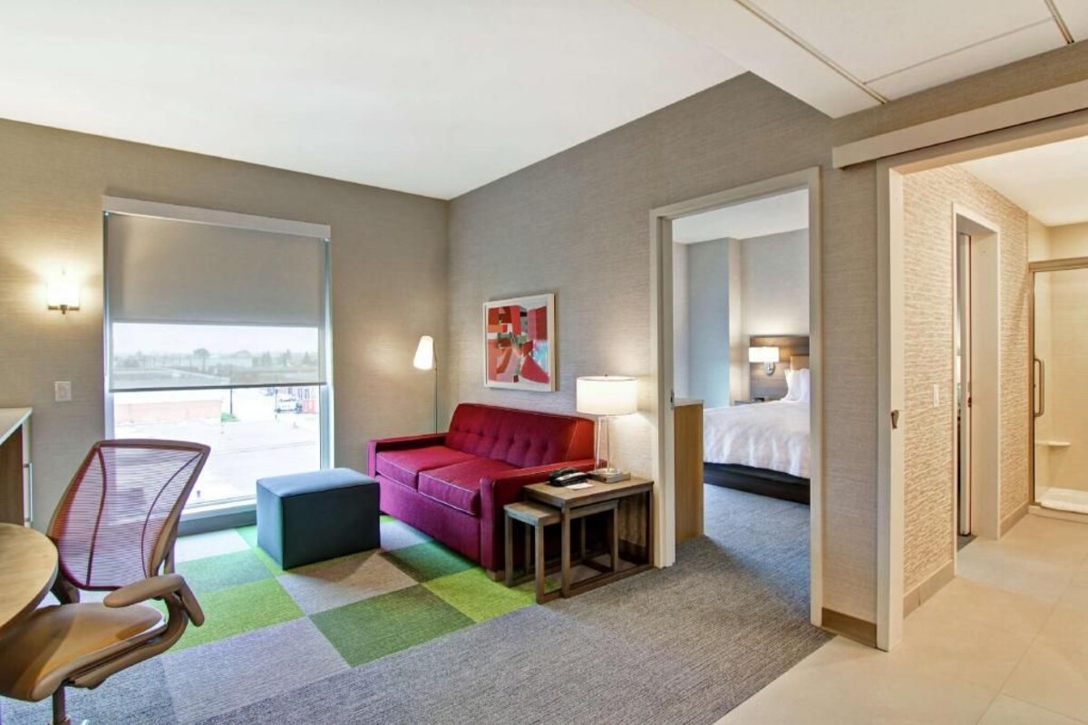 Een hotelkamer met een rode bank, een kleine tafel, een lamp, een bed en een raam met uitzicht.