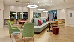Een moderne zithoek met een bank, groene fauteuils met een patroon, een eettafel en hanglampen.