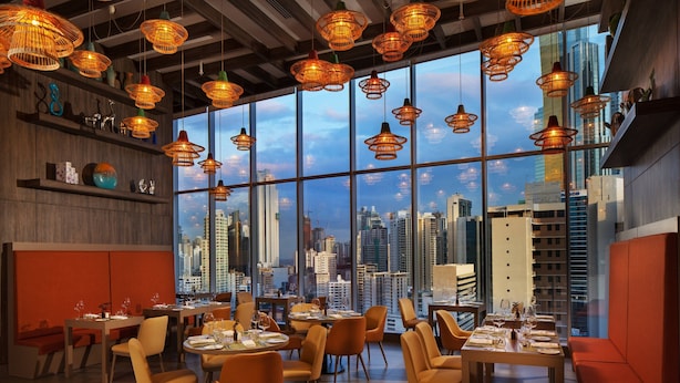 A modern restaurant with large windows offering a city view, warm lighting, and contemporary furniture. - W Panama (Panama City)