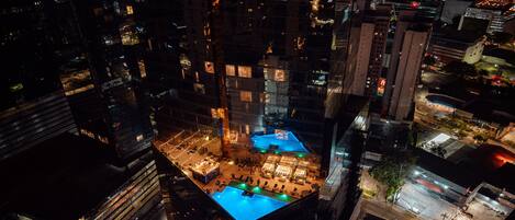 A high-rise building with a rooftop pool area, surrounded by other buildings.